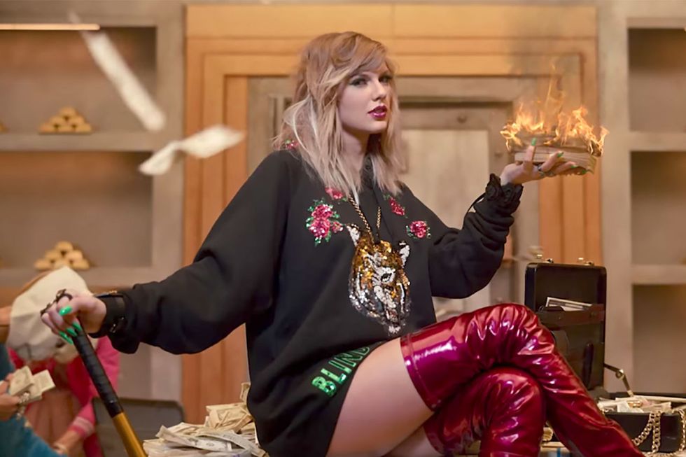 <p>Very cold from not wearing pants, bank-robbing Taylor sets fire to a pile of cash to keep warm, while showing off her bedhead-y waves and glitter-flecked burgundy lips.</p>