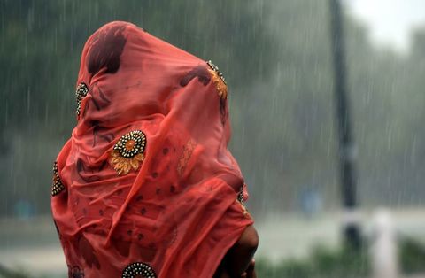 An Indian woman covers her baby under her saree during heavy rain at Rajpath in New Delhi on August 7, 2017 | ELLE UK