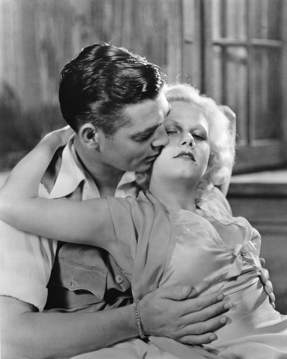 <p>Jeans Harlow, de eerste blonde bombshell ooit, werd ontzettend populair in de jaren 30, nog voor het Pre-Code tijdperk van Hollywood. Ze hield ervan om jurken in bepaalde stoffen te dragen die plakten rondom haar boezem. Om nog extra te 'shockeren' droeg ze geen beha. Het beeld is een still - met Clark Gable -uit de film Red Dust. </p>