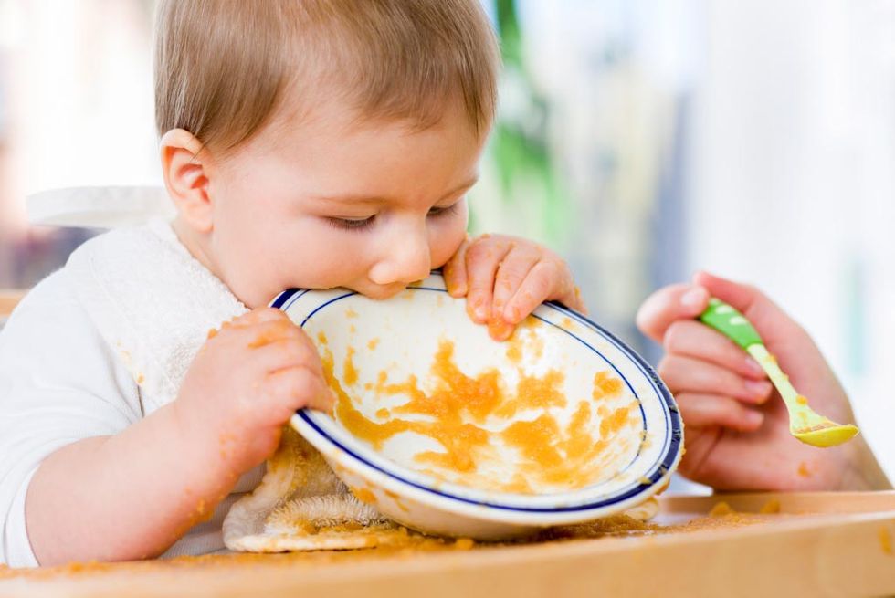 bebé mordiendo el plato del puré de verduras después de haberlo terminado