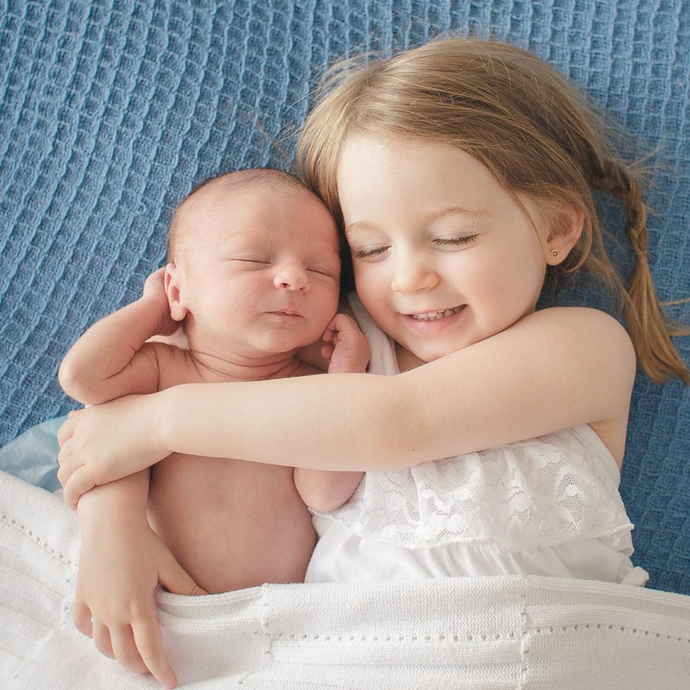 un bebé recién nacido duerme abrazado por su hermana mayor