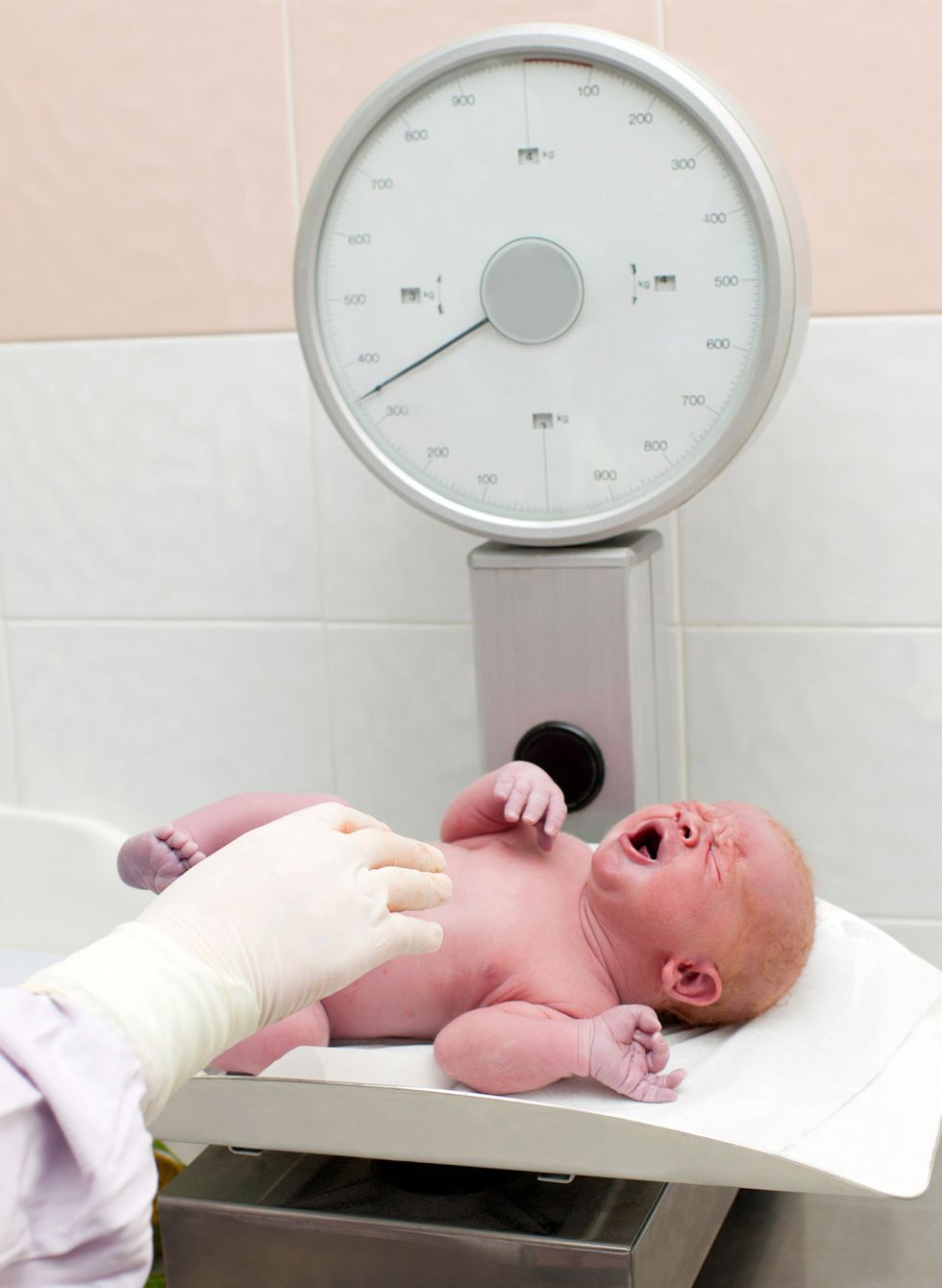 un médico pone al bebé  en la báscula para controlar la curva de peso del recién nacido