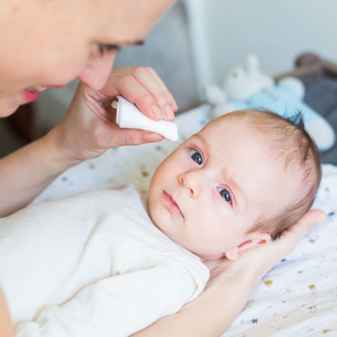 una madre limpia los ojos de su bebé con conjuntivitis con una gasa
