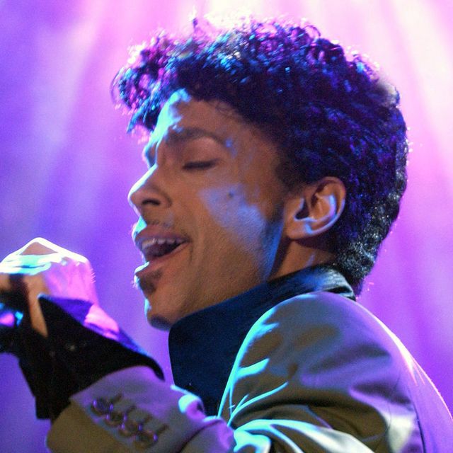 Prince holds a microphone and sings; purple lights are in the background