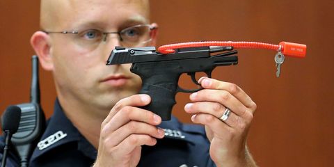 a police officer in court holds the gun that shot Trayvon Martin