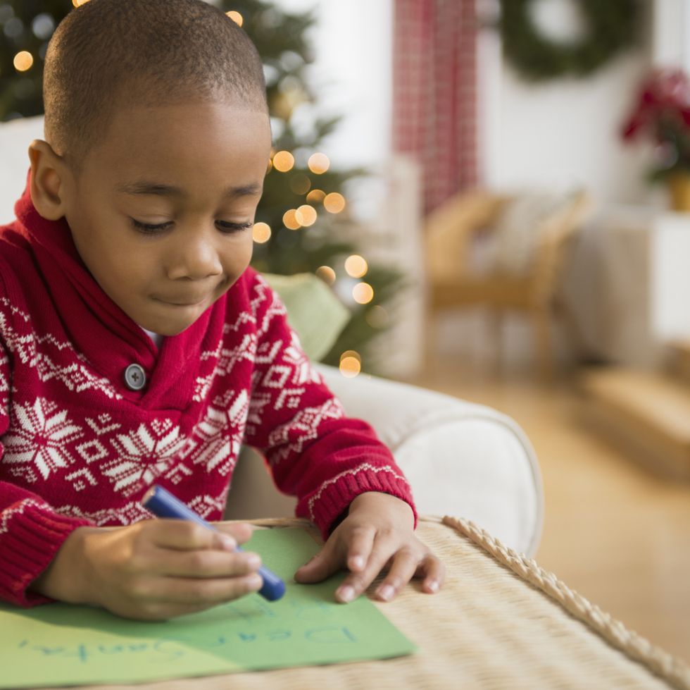 black boy writing letter to santa while wearing a red and white sweater