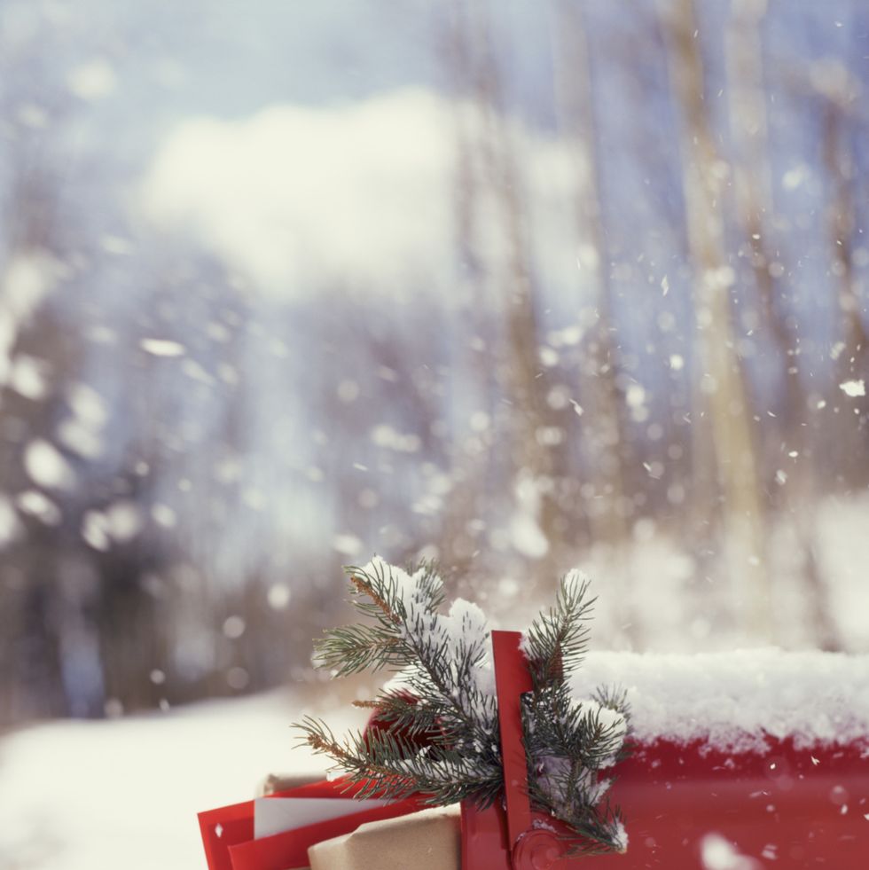 a red mailbox with evergreen and stuffed full of mail in the snow