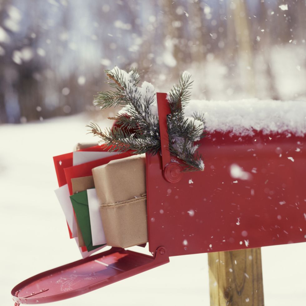 a red mailbox with evergreen and stuffed full of mail in the snow