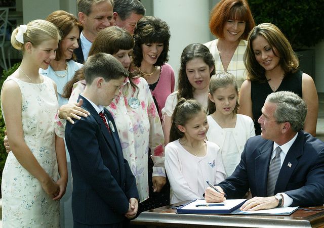 Rodeado por las familias de las víctimas secuestradas, incluyendo a Elizabeth Smart (L), sus padres Lois y Ed, y Donna Norris, la madre de Amber Hagerman, el presidente de EE.El Presidente de los Estados Unidos, George W. Bush (derecha), firma la ley de Alerta Amber en el Jardín de las Rosas de la Casa Blanca el 30 de abril de 2003 en Washington, DC. El plan nacional de 