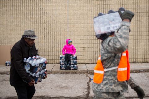 Zariah Garner, age 9 of Flint, rests on a stack of water as national guard members and civilians carry cases to vehicles on January 23, 2016 in Flint, Michigan. Water is being handed out for free to citizens of Flint after a federal state of emergency was declared over the city's contaminated water supply.