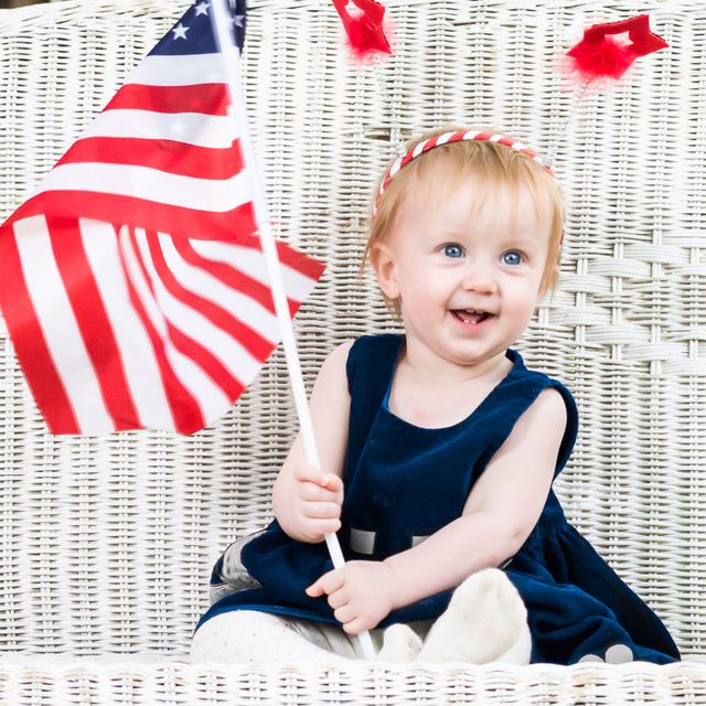 Baby on white wicker bench holding American flag