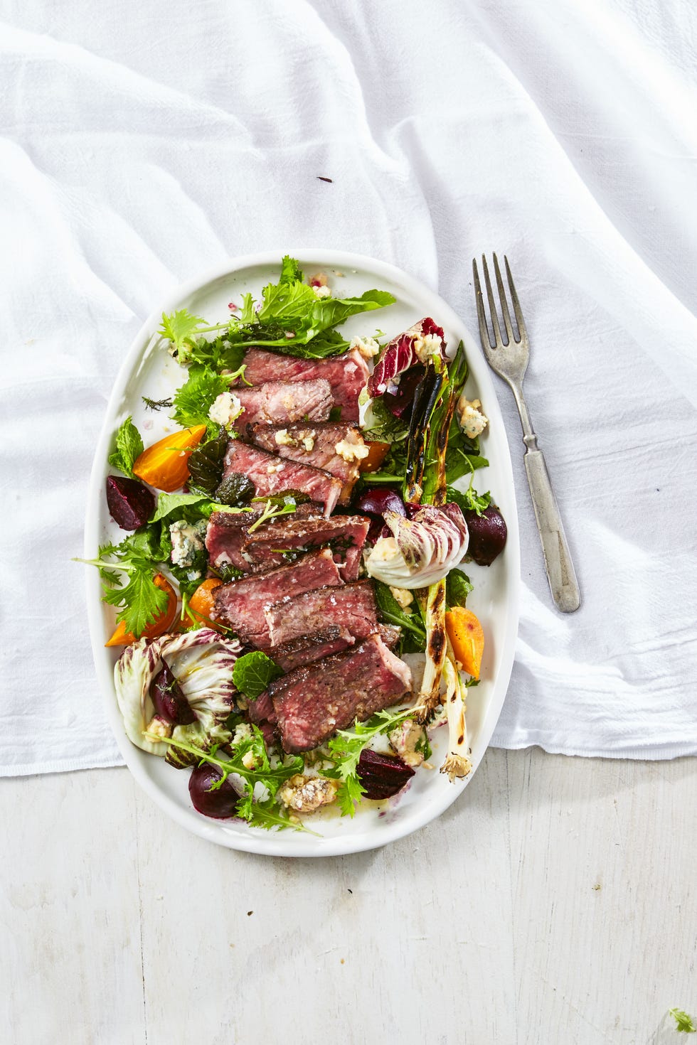 steak salad with charred green onions and beets on a white plate