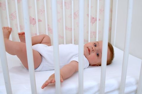 baby lying in white crib with pink butterfly wallpaper in the background