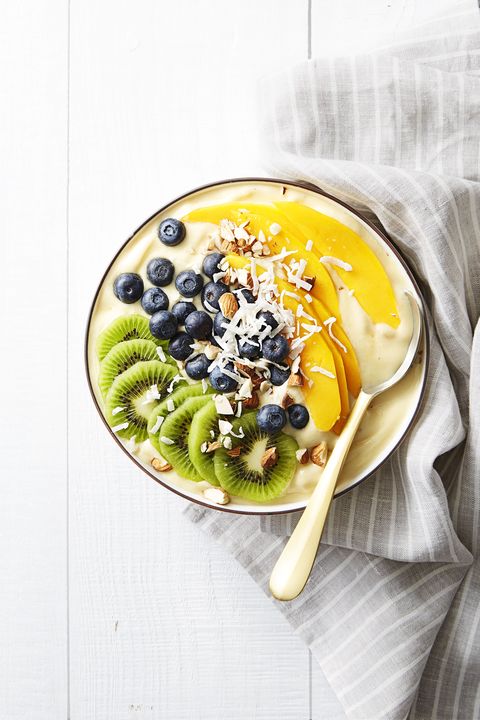tropical smoothie bowl with mango, blueberries, kiwi, and coconut shavings on a wooden table
