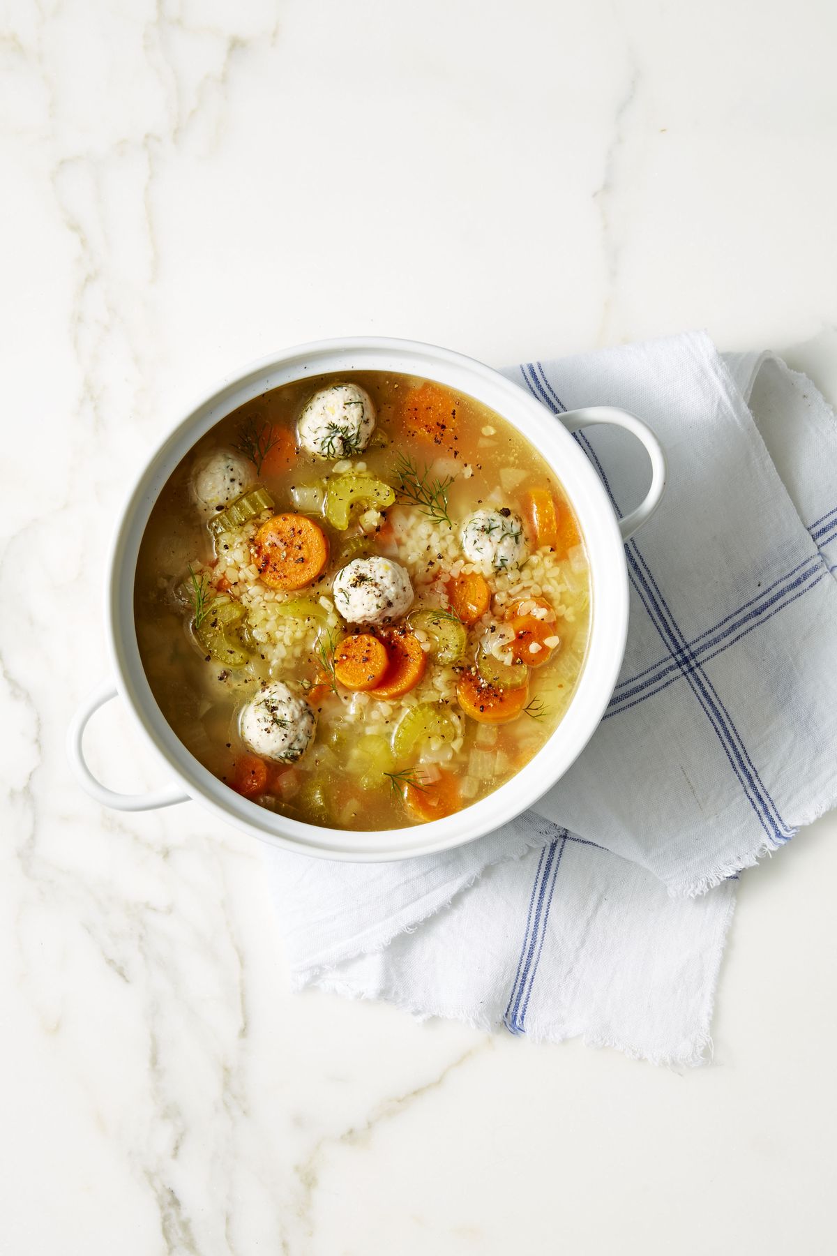 lemon dill chicken meatball soup with sliced carrots in a white pot
