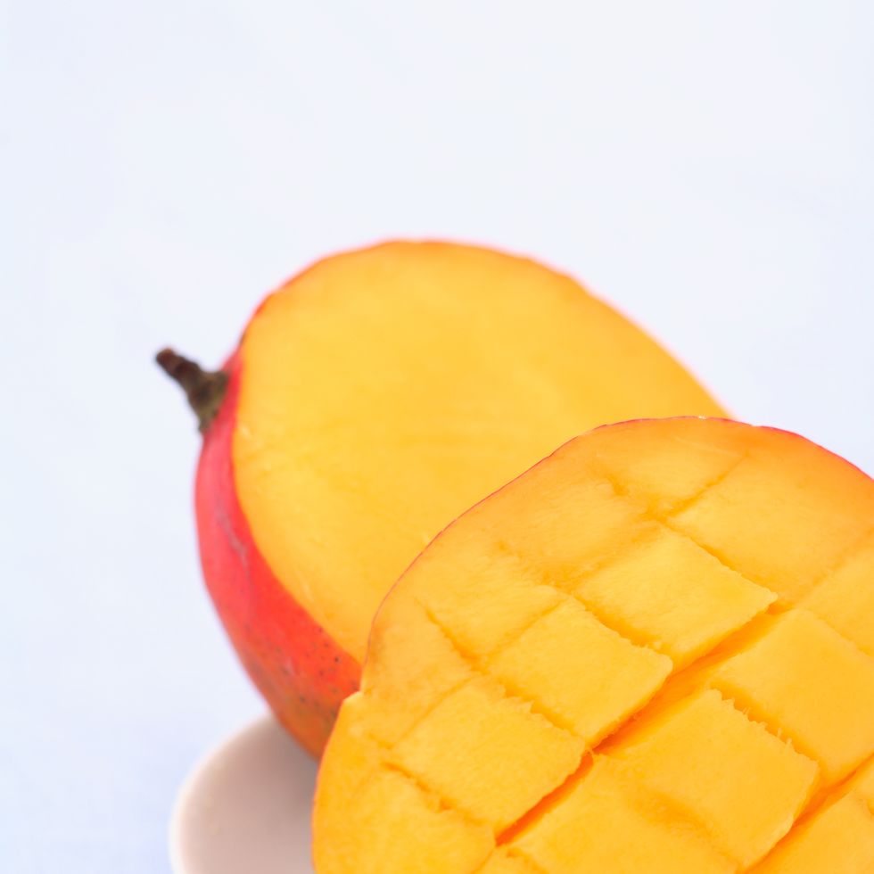 mango cut in half on a white plate and blue backdrop