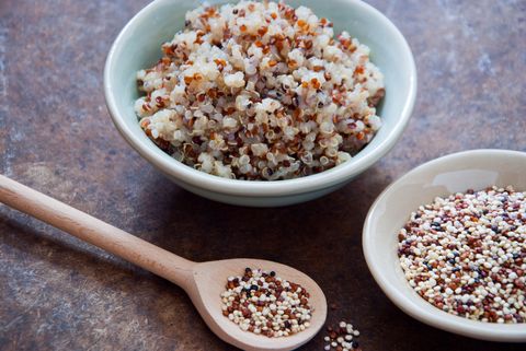a bowl of cooked quinoa and a spoon of raw quinoa on a brown background, a good housekeeping pick for healthy weight loss food