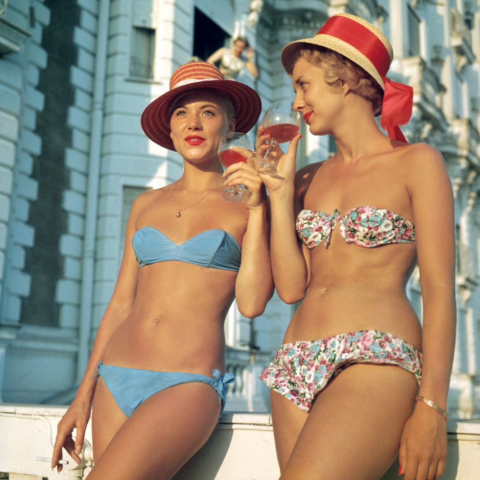 Premium Rates Apply. Two bikini-clad holidaymakers enjoy a glass of wine outside the Carlton Hotel, Cannes.  (Photo by Slim Aarons/Getty Images)