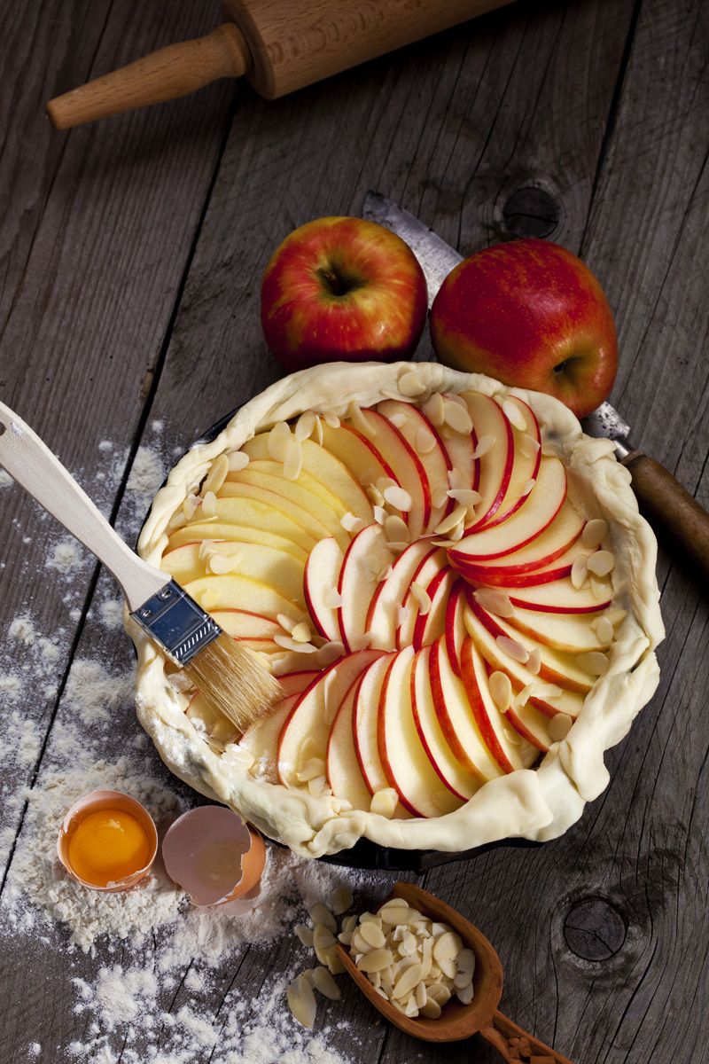 Raw apple pie in cake pan and ingredients on wood
