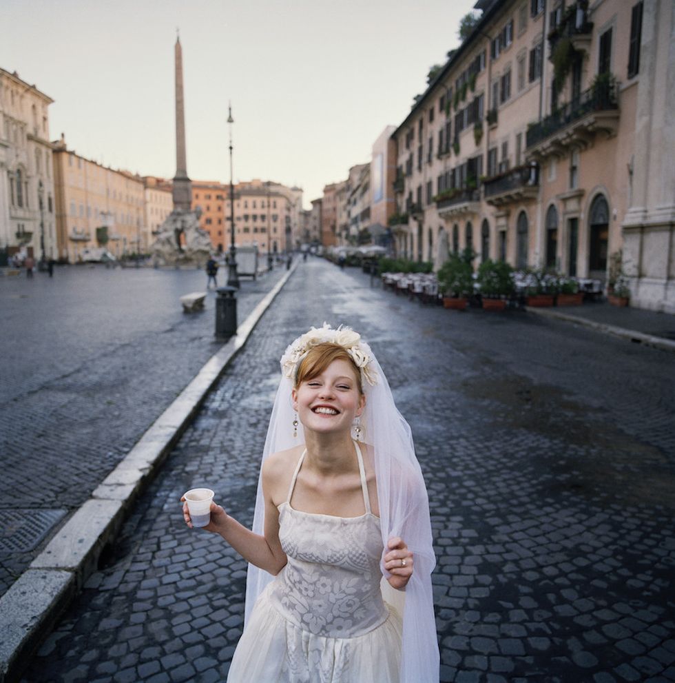 sposa felice con abito bianco e velo fotografata in strada