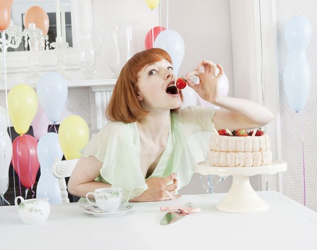 una ragazza mangia un fragola da una torta di pasticceria