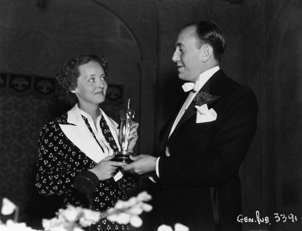 <p>Bette Davis picks up the first of her ten eventual Best Actress awards (this one for <i data-redactor-tag="i">Dangerous</i>) from producer Jack Warner. Forced by Warner to attend the awards instead of take a vacation, Davis selected an outfit—a costume from a Warner film that had failed—that she hoped he would recognize.<span class="redactor-invisible-space" data-verified="redactor" data-redactor-tag="span" data-redactor-class="redactor-invisible-space"></span></p>