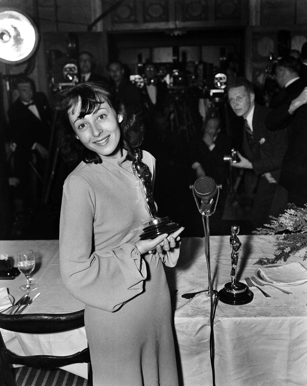 <p>The lovely Luise Rainer becomes the first actor to win an award in two consecutive years, this time for <i data-redactor-tag="i">The Good Earth, </i>and again attends the awards without makeup but has found a formal gown.<br></p>