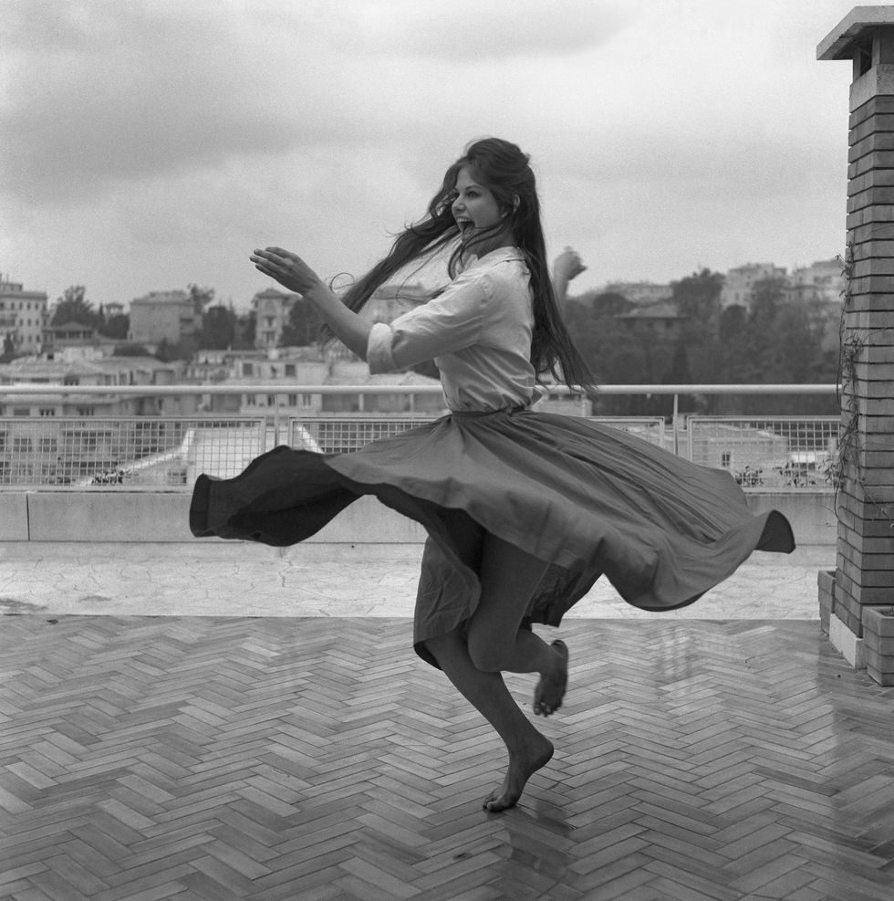 Italian actress Claudia Cardinale, wearing a shirt and a wide skirt, dancing barefoot on a roof terrace in Rome, 1959