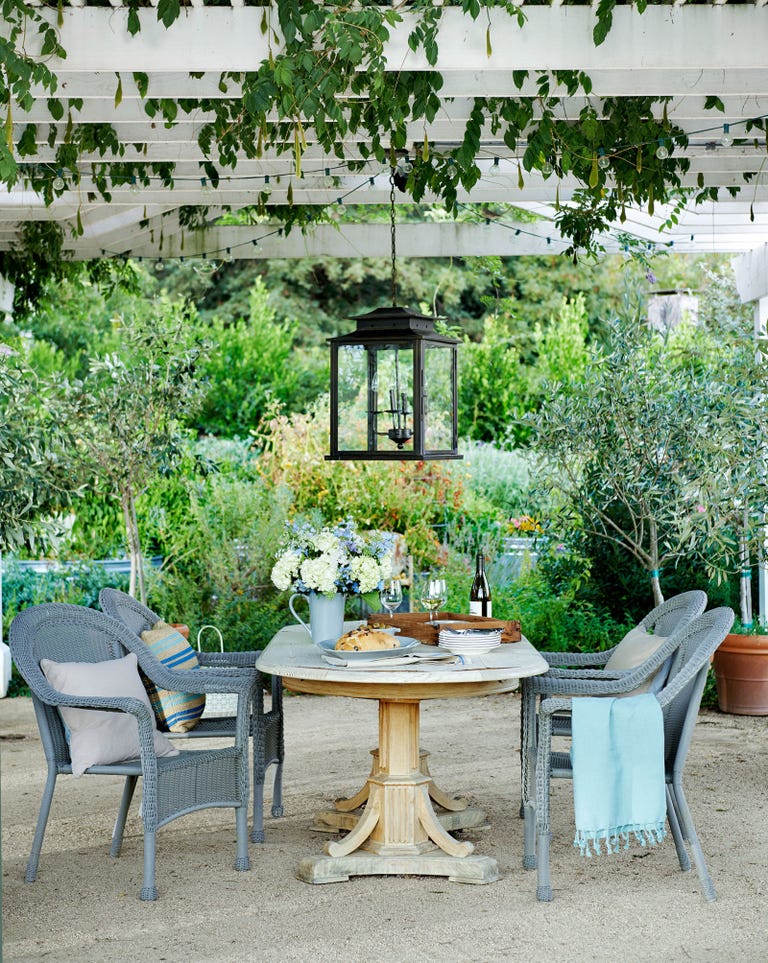 Wicker chairs from Target pull up to an antique pine table under a wisteria-covered pergola at a farmhouse in California. #outdoordining #pergola #outdoorliving #lantern