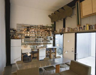 Functional Kitchen kitchen with steel table top and shelving above sink and oven as well as a book shelf above doors and chairs hanging on wall