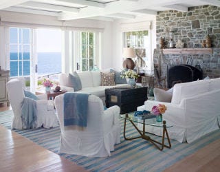 living room with large stone fireplace and white slip covers on furniture and blue striped run