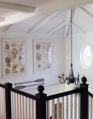 upstairs hallway with black banister and black chandelier near an oval window