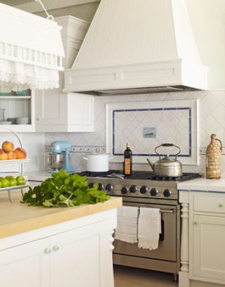 white kitchen viewing the stove with teapot and white hood above