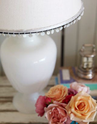 white lamp with sea shell fringe on edge next to rose bouqet