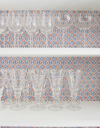wine glasses inside cabinet with paper-lined wall in background