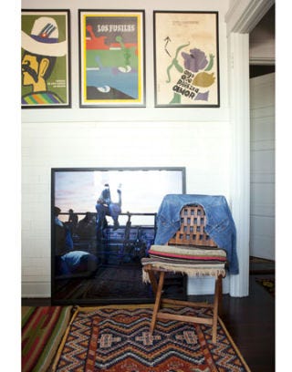 corner of a kitchen with vintage posters hanging and a large photograph propped up next to a chair