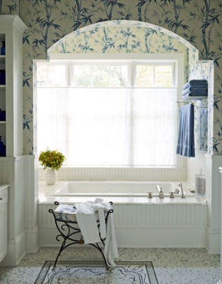 a blue and white bathroom with bamboo patterned wallpaper and a large white tub next to the window