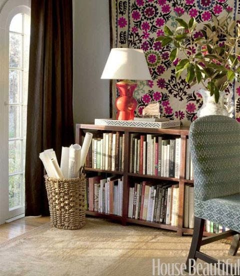 a textile hung above a bookcase with a red lamp on the wall in office