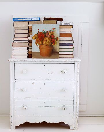 a white antique dresser with books on it with a painting in front