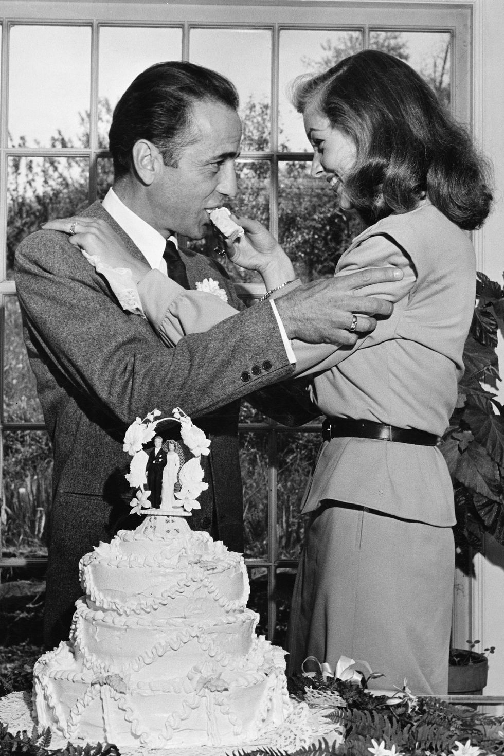 Actress Lauren Bacall feeding cake to husband Humphrey Bogart at their wedding at Louis Bromfield's farm.