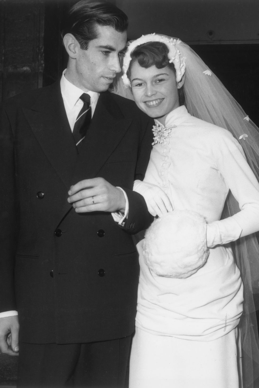 20th December 1952:  French actor Brigitte Bardot smiles and leans her head on the shoulder of her husband, French film director Roger Vadim (1928 - 2000), on their wedding day at the Church of Passy, France. She wears her wedding dress and veil, with one hand in a muff.  (Photo by RDA/Getty Images)