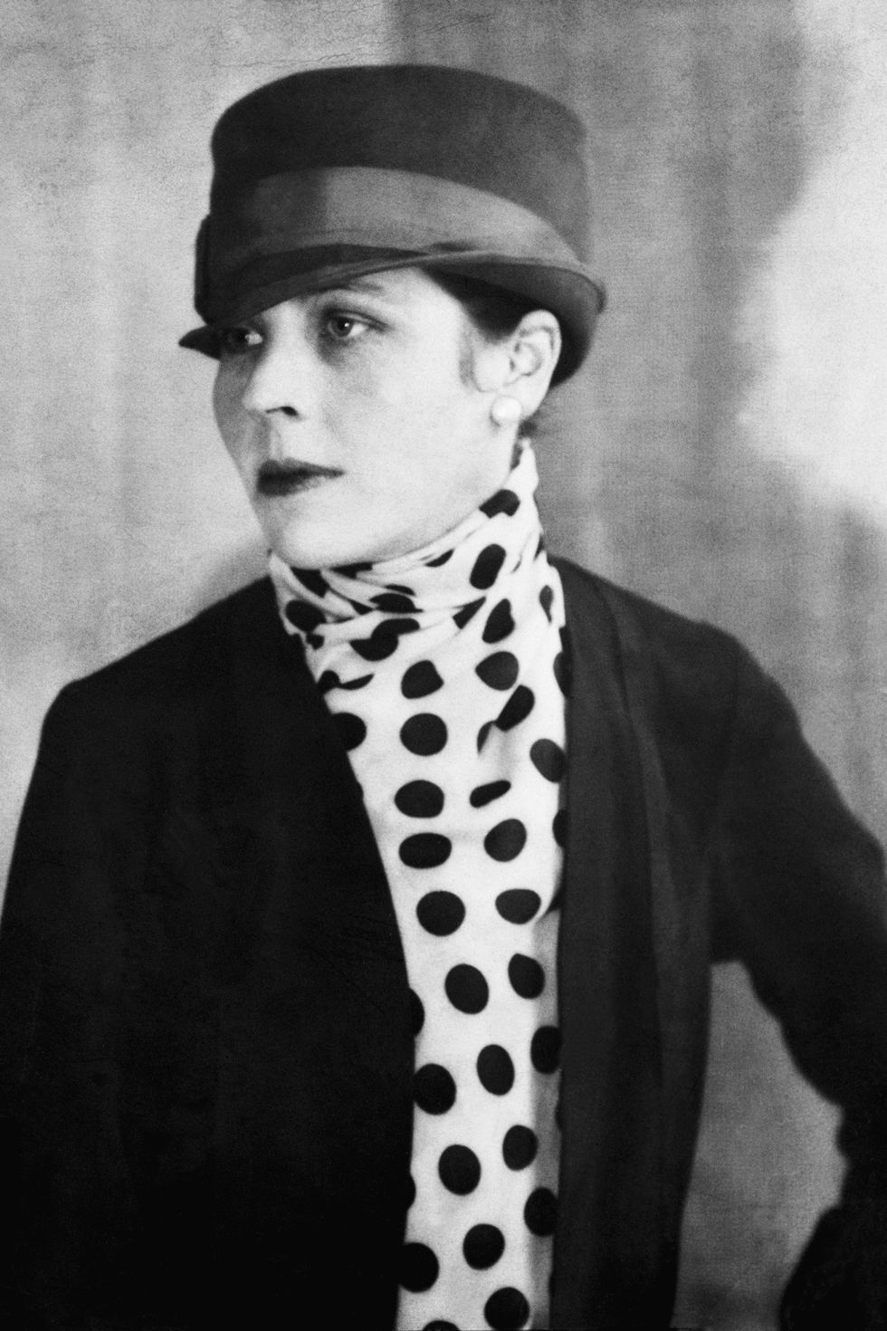 <p>As a poet, journalist, playwright and visual artist, Djuna Barnes is best known for her novel, <em>Nightwood</em>. She is considered a modernist, writing from both New York City and Paris—which inspired her style. She favored prints, in the form of bold polka dots—dramatic capes, and metallic turbans. She wrote under the penname of "A Lady of Fashion".</p>