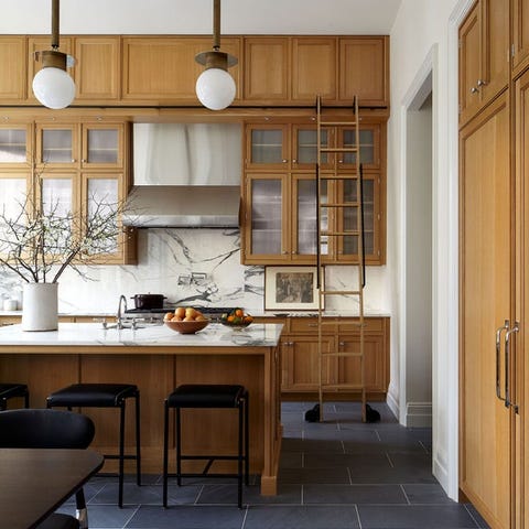 A List 2022 - ELLE DECOR bamboo kitchen with rolling ladder and center counter with low stools tucked under and a blue tile floor