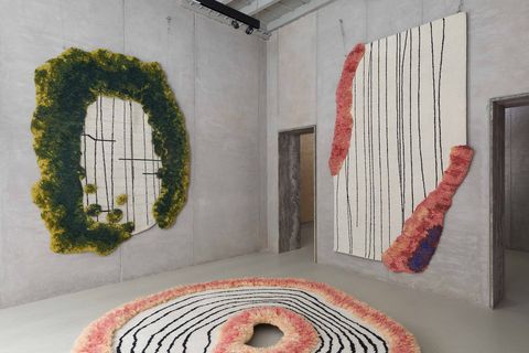 a room with grey walls with two rugs on the wall and one on the floor one on the wall is surrounded by green with stripes the other is striped with pink fuzzy borders and the circular one on the floor has a pink fuzzy border and center