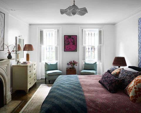 quarto, poltronas azuis, roupa de cama vermelha, colcha verde, almofadas decorativas, lareira, luz de teto branca