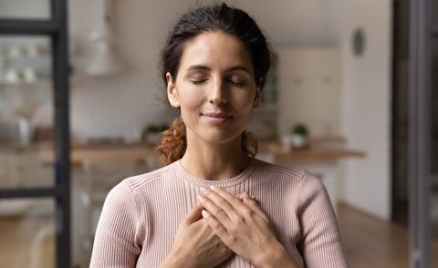 close up of calm young caucasian woman hold hands on heart chest feel grateful and thankful happy millennial female show gratitude, love and care, pray or visualize religion, faith concept
