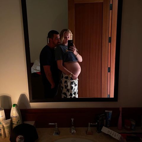 pregnant sophie turner taking a mirror selfie while cradling her exposed belly with joe jonas standing over her shoulder
