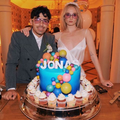 sophie turner and joe jonas posing stoically in matching sunglasses in front of a giant cake with 