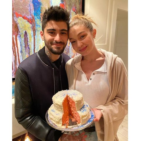 zayn malik and gigi hadid stand smiling with a pink cake in between them