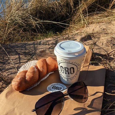 a takeaway coffee cup and a pastry on sand by the sea